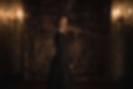 A woman stands in a dim Victorian hallway with candlelight.