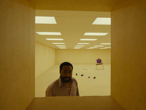 A person stands in a yellow, empty room under fluorescent lights.