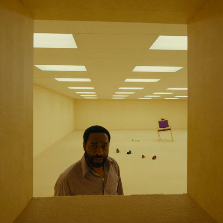 A person stands in a yellow, empty room under fluorescent lights.