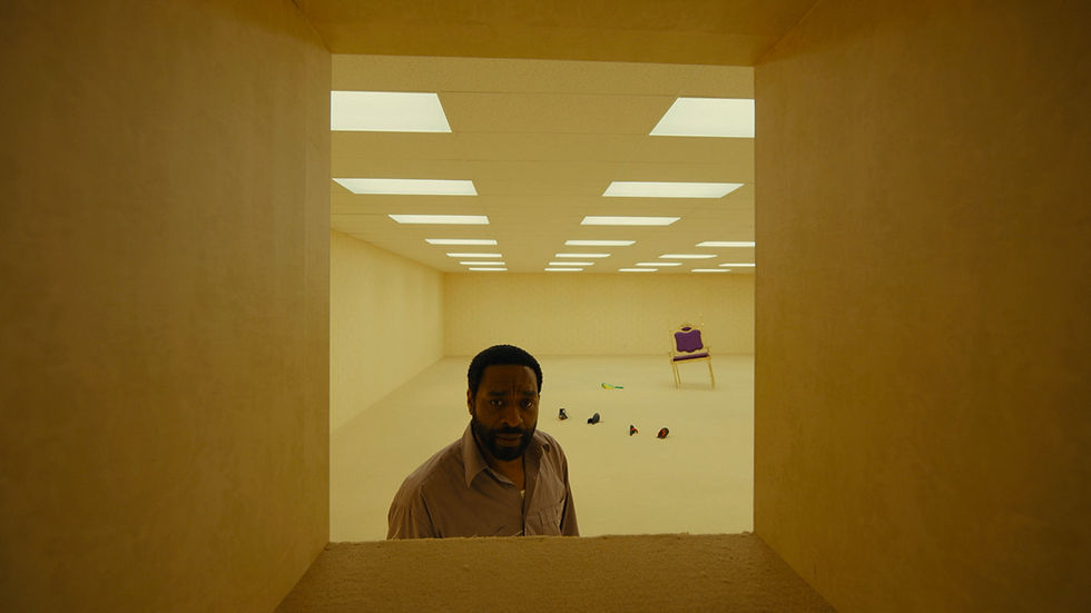 A person stands in a yellow, empty room under fluorescent lights.