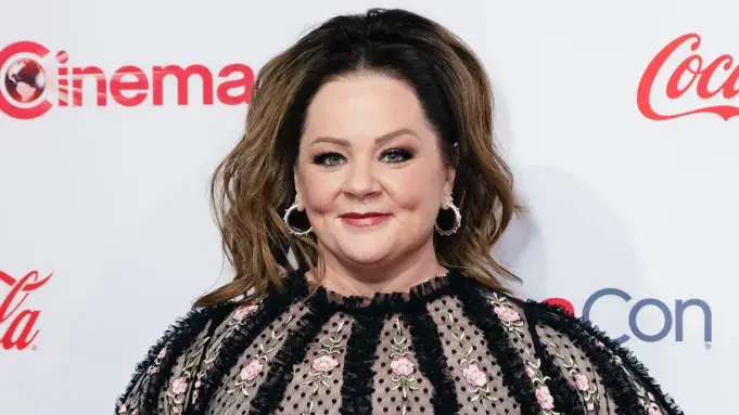 A woman looks serious in a dimly lit dramatic setting.