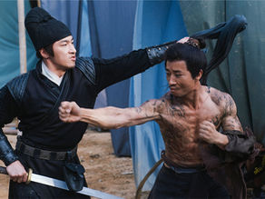 A warrior holds a sword in a tense wuxia battle scene.