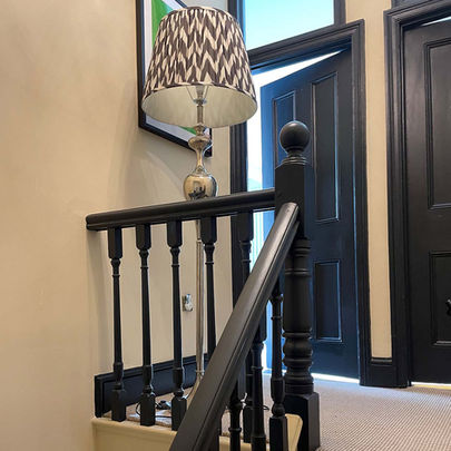 Professionally painted stairwell with cream walls, navy doors, matching door frames, skirting boards and bannister, leading to a carpeted landing with two doors.