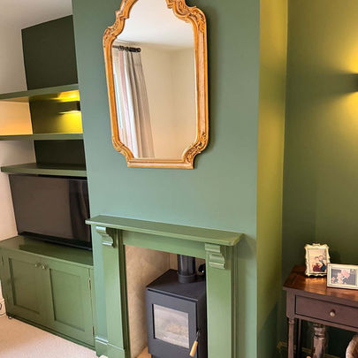 Professionally painted lounge in a terraced house with green alcoves, chimney breast, fire surround, shelving, panelled cupboard and skirting boards, contrasted against cream walls and carpet.