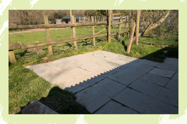 Sunny backyard with a tiled patio, wooden fence, and grass. Yellow cable runs along the fence. Shadow creates a zigzag pattern.