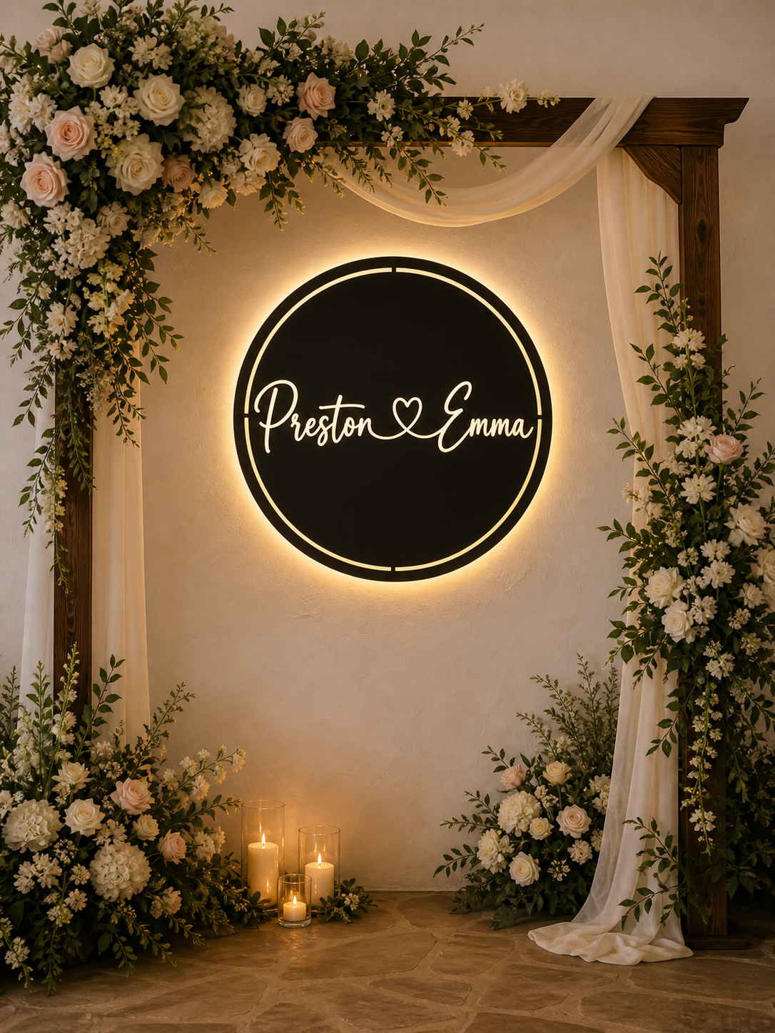 Backlit round metal wedding sign with Preston and Emma in connected cursive script, displayed on off-white wall with flowers