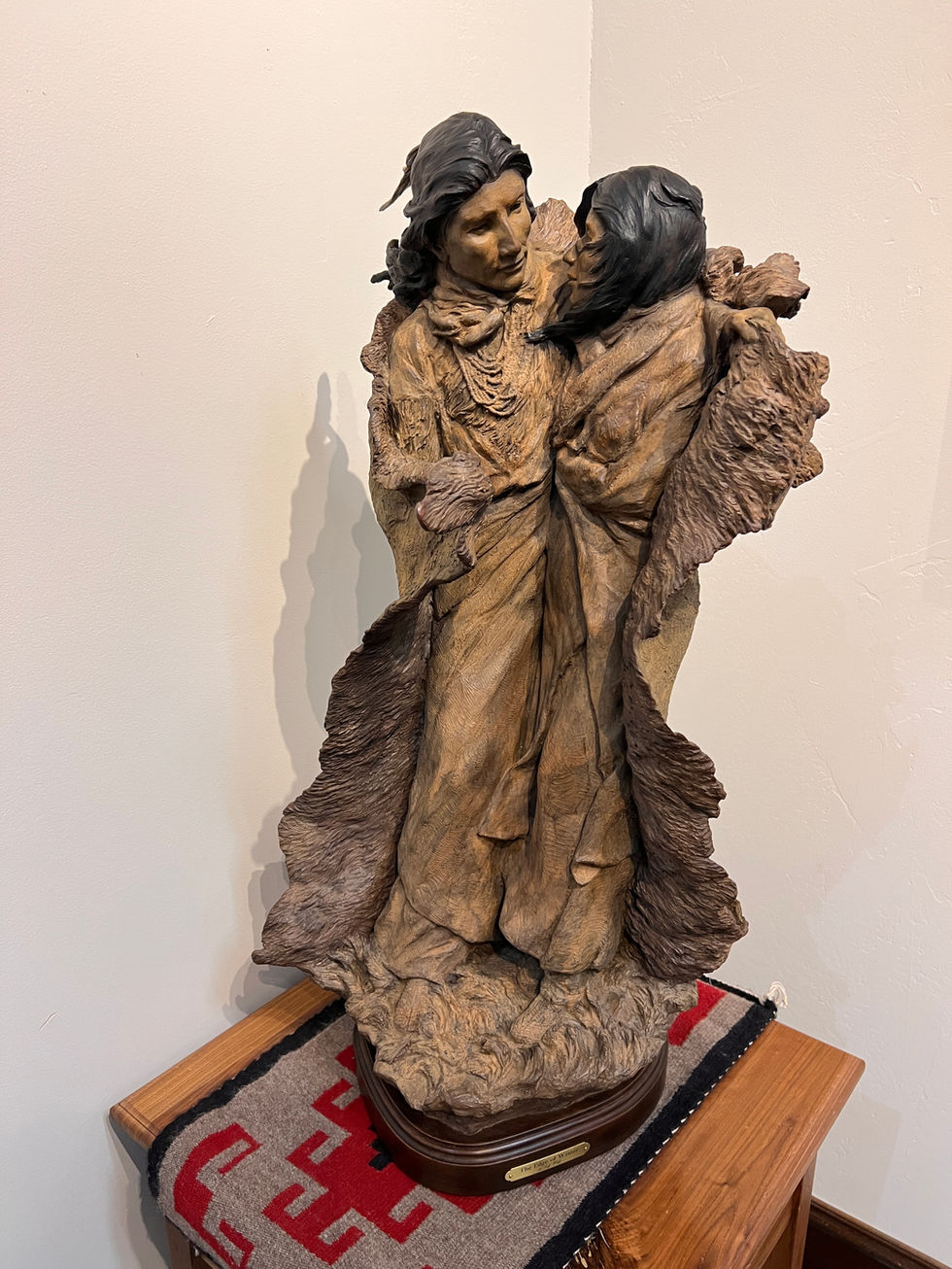 a statue of two native people standing next to each other with a blanket wrapped around them, gold river gallery, bronze sculpture