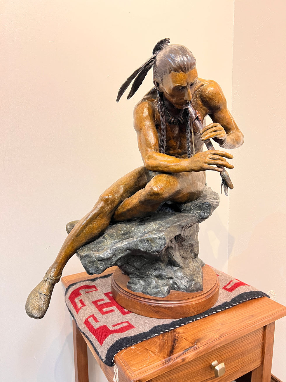 a bronze statue of an Indian man sitting on a rock, playing a flute. Bronze Sculpture, Gold River gallery