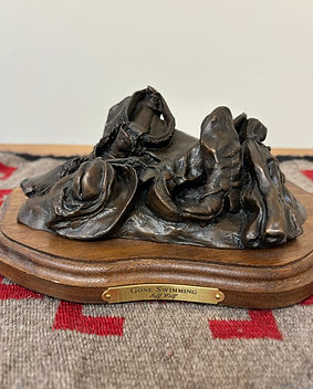 Bronze sculpture by Jeff Wolf of a cowboy who left all of his riding gear and clothes in a pile to go swimming 