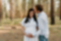 An expecting mother is looking down while holding her baby bump. Her husband is ksising her on the cheek as they pose for the camera during their maternity session.