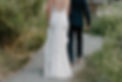 A bride and groom hold hands walking together with their backs to the camera.