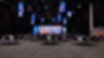 Corporate event with prominent LED wall displays on the ceiling, stage, and as scenic design, with speakers presenting to an assembled audience.