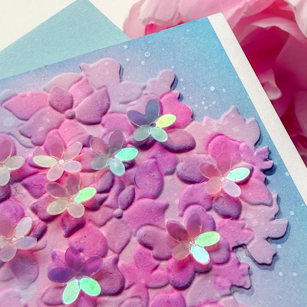 Close-up of a handmade pink and purple floral card with shiny sequins on a blue background, soft and whimsical mood