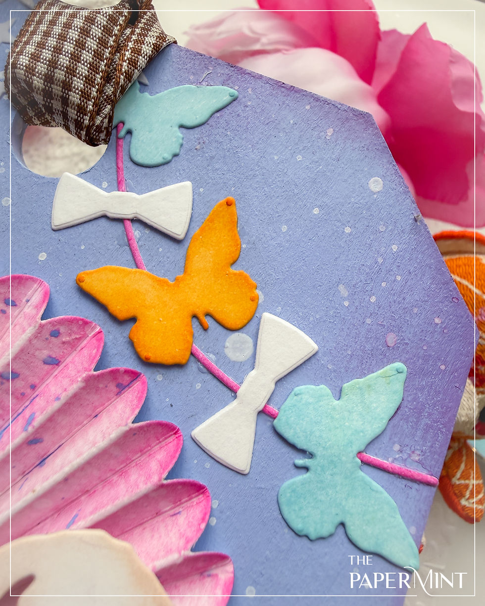 Blue textured paper with colorful butterfly and bow cutouts. Pink flower decor and "The Papermint" text. Bright and cheerful design.