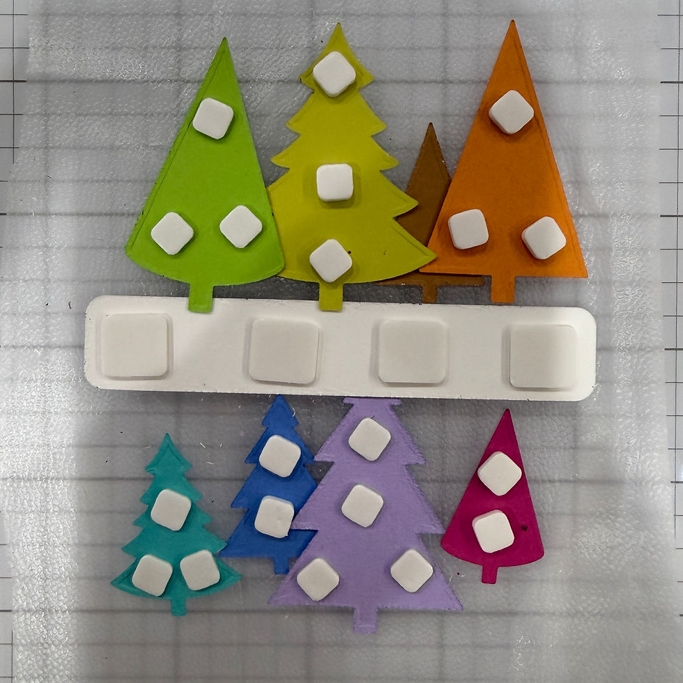 Backs of colorful tree die-cuts and a long sentiment strip with white square foam adhesive pieces attached.