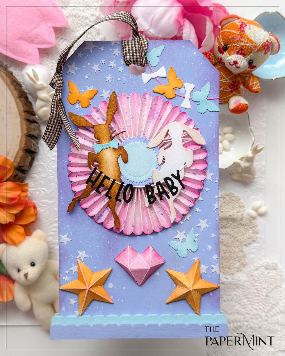 Blue and pink baby nursery decor with rabbits, butterflies, stars, and "HELLO BABY" text. Features gingham ribbon. Background shows floral décor.
