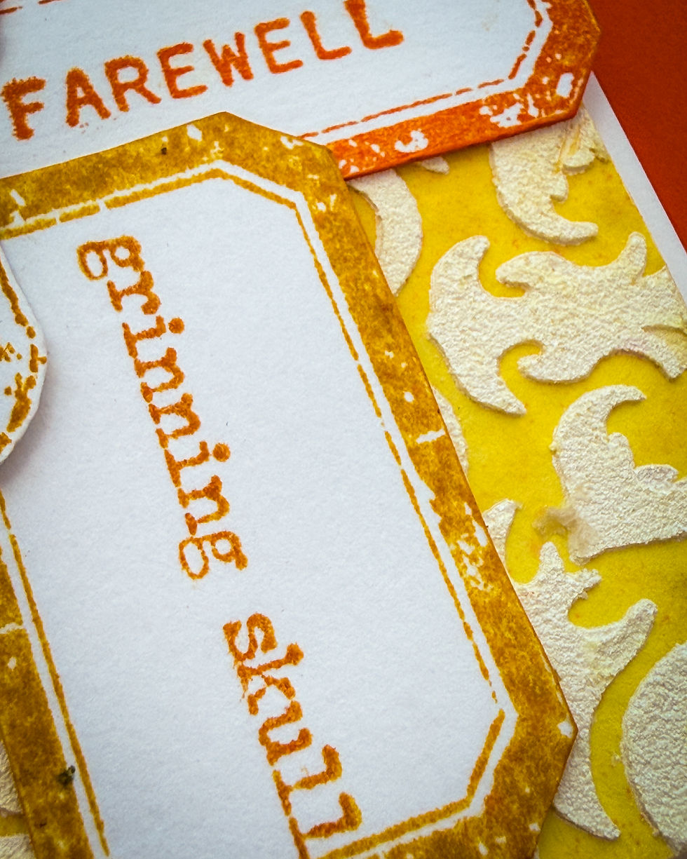 Close-up of yellow and white decorative paper labels with orange text, including Farewell and Good Wishes, overlapping.