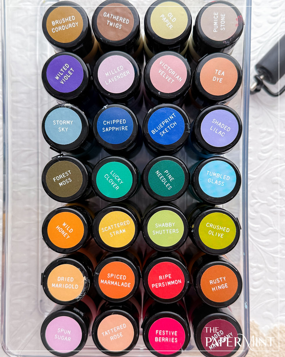Colorful ink bottles with labels like Brushed Corduroy and Stormy Sky arranged in rows. White textured background. Mood is creative.