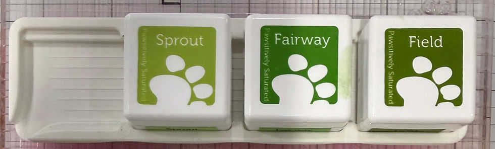 Three white square ink pads on a white tray against a grid background. Labeled "Sprout," "Fairway," and "Field" with green designs.