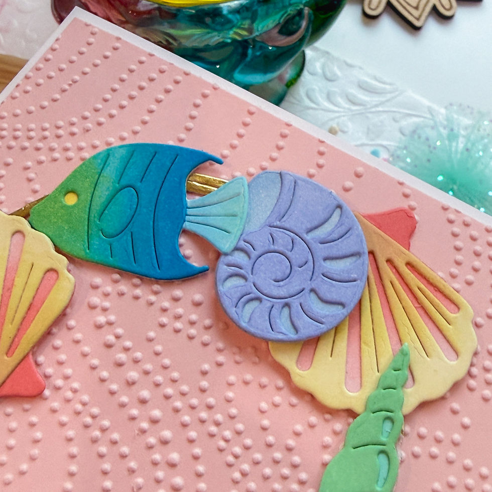 Colorful fish and spiral shell craft on a pink textured background, with pastel cutouts and a playful, handmade look