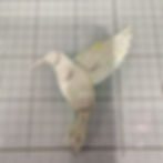 Paper hummingbird craft with green patterns on a gridded cutting mat.