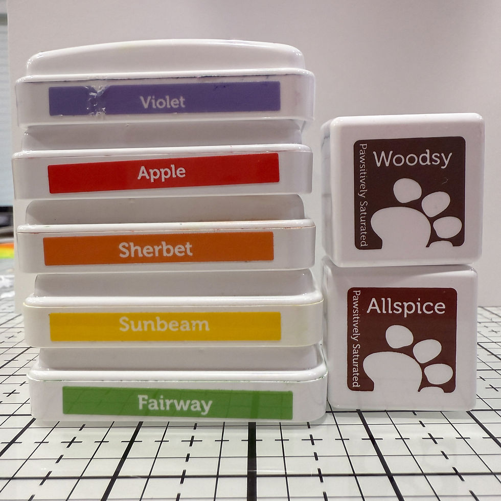 Stack of colorful ink pads labeled Violet, Apple, Sherbet, Sunbeam, Fairway, Woodsy, Allspice on grid surface. Bright and organized.