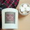 Thumbnail: Flannel Warm Fall Candle Flat Lay on Beige Table with Red Flannel Blanket and Cup of Hot Cocoa Topped with Marshmallows