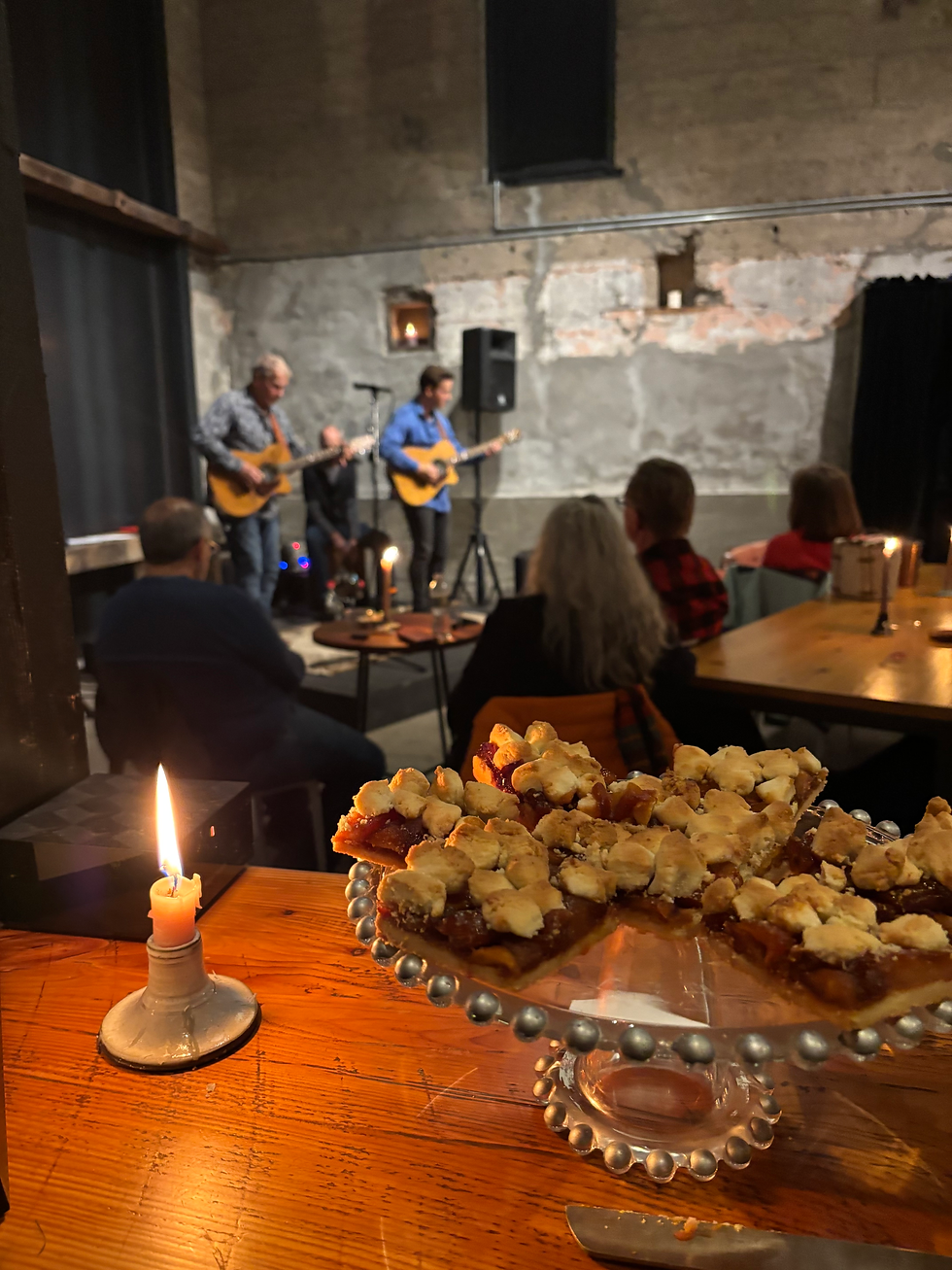 Father and son duo play acoustic guitars on state against a black barn door