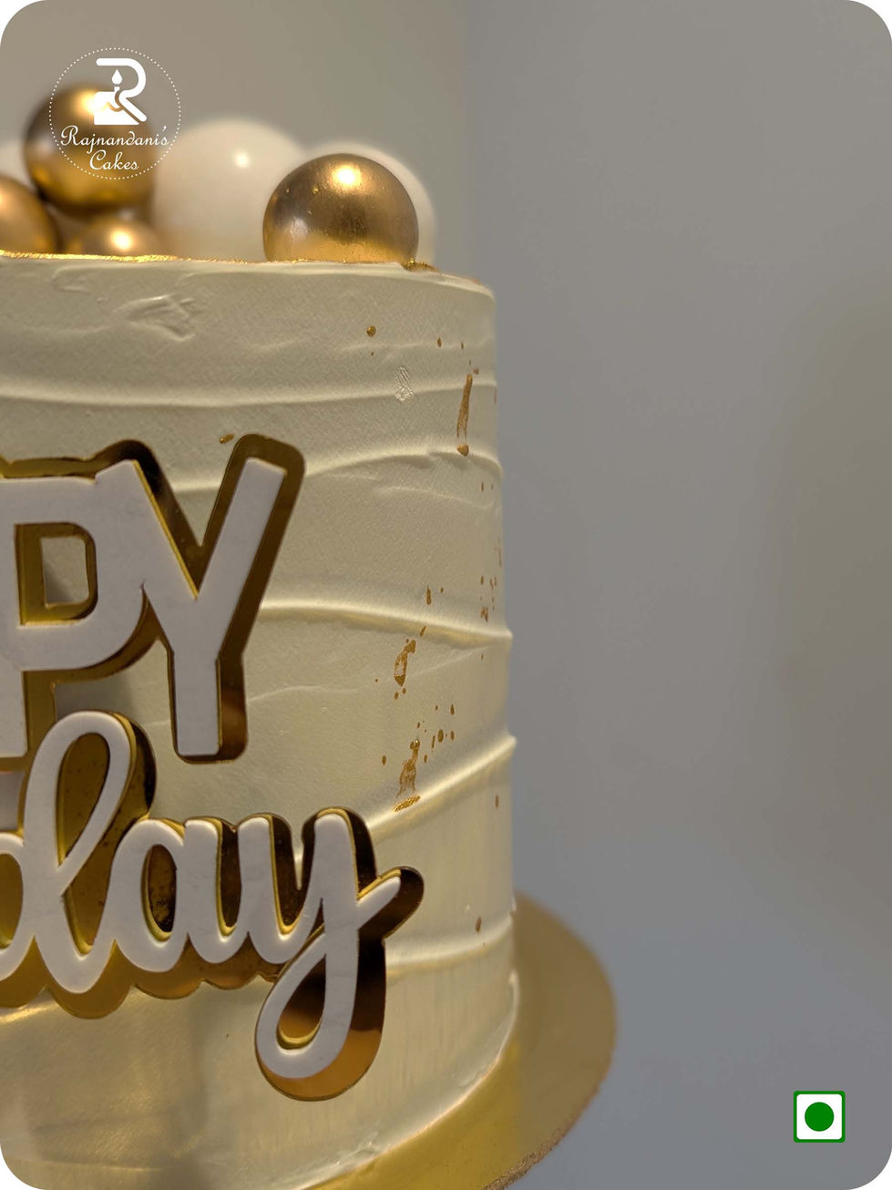 Textured white Whipping cake decorated with gold leaf splatters, white and metallic gold chocolate spheres, tall wavy gold