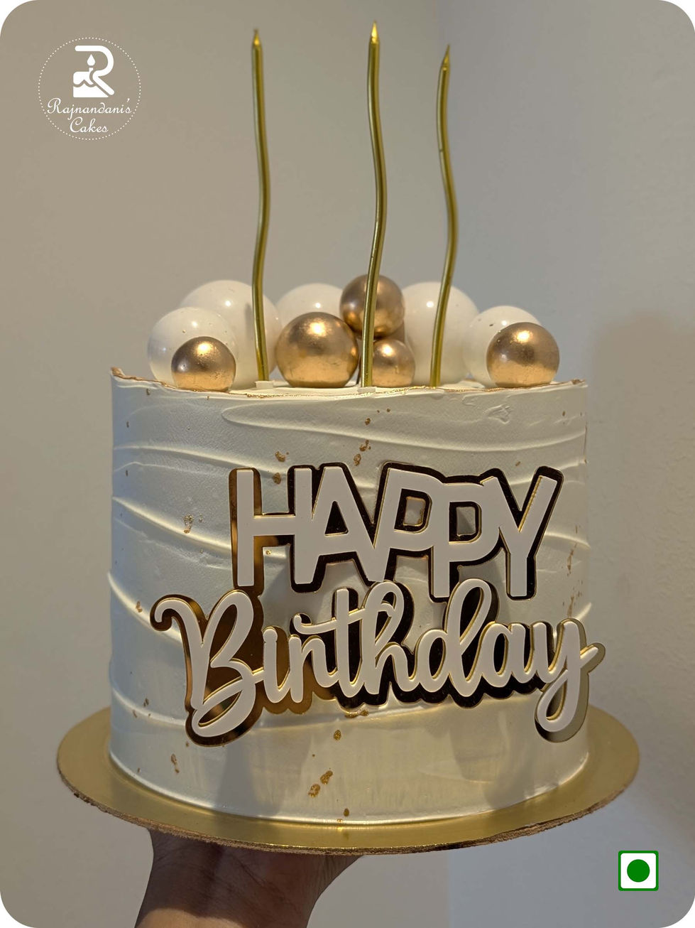 Textured white Whipping cake decorated with gold leaf splatters, white and metallic gold chocolate spheres, tall wavy gold