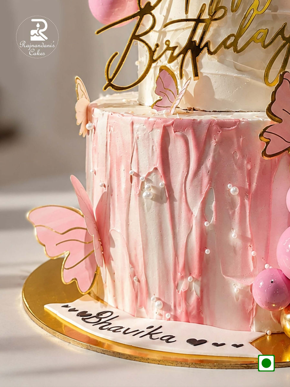 Two-tier pink and white birthday cake adorned with flutter butterflies, gold and pink spheres, and acrylic topper.