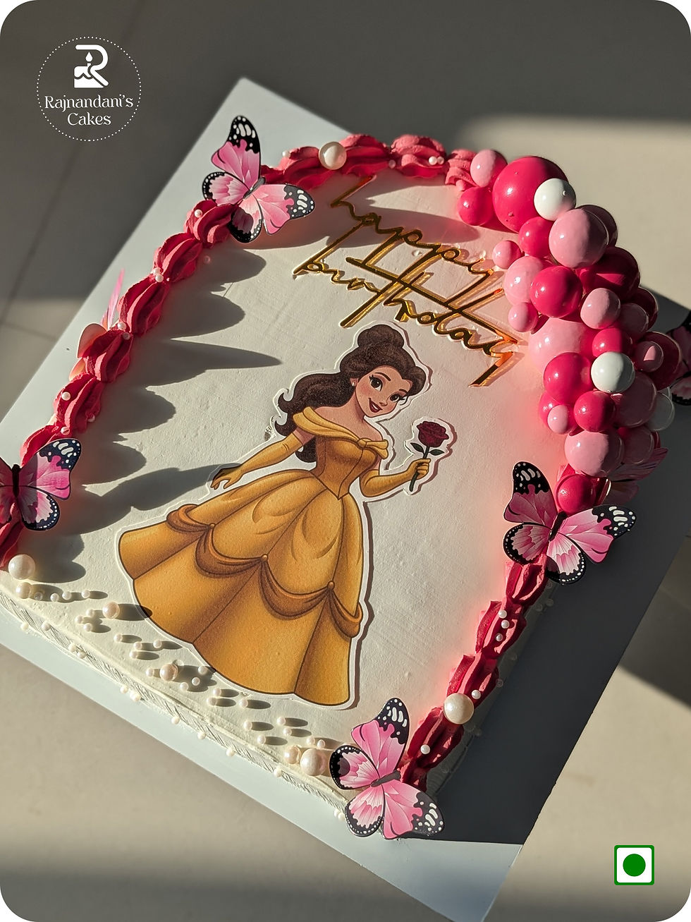 Rectangular princess cake featuring a Princess Belle topper, pink butterfly cutouts, and faux balls arch by Rajnandani's