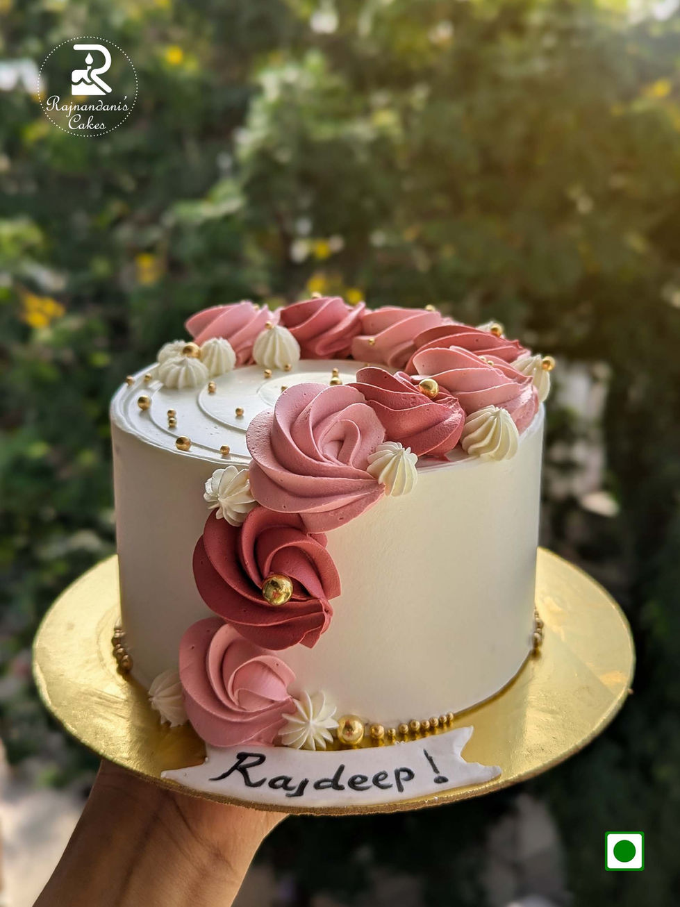 White whipped cream cake decorated with cascading dusky pink piped rosettes, cream swirls, and shiny gold edible pearls.