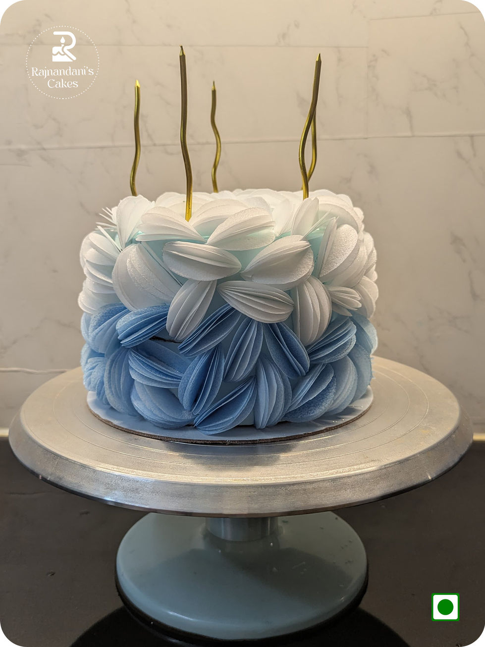 blue and white ombre cake sculpted with edible delicate wafer paper petals and metallic candles by Rajnandani's Cakes.