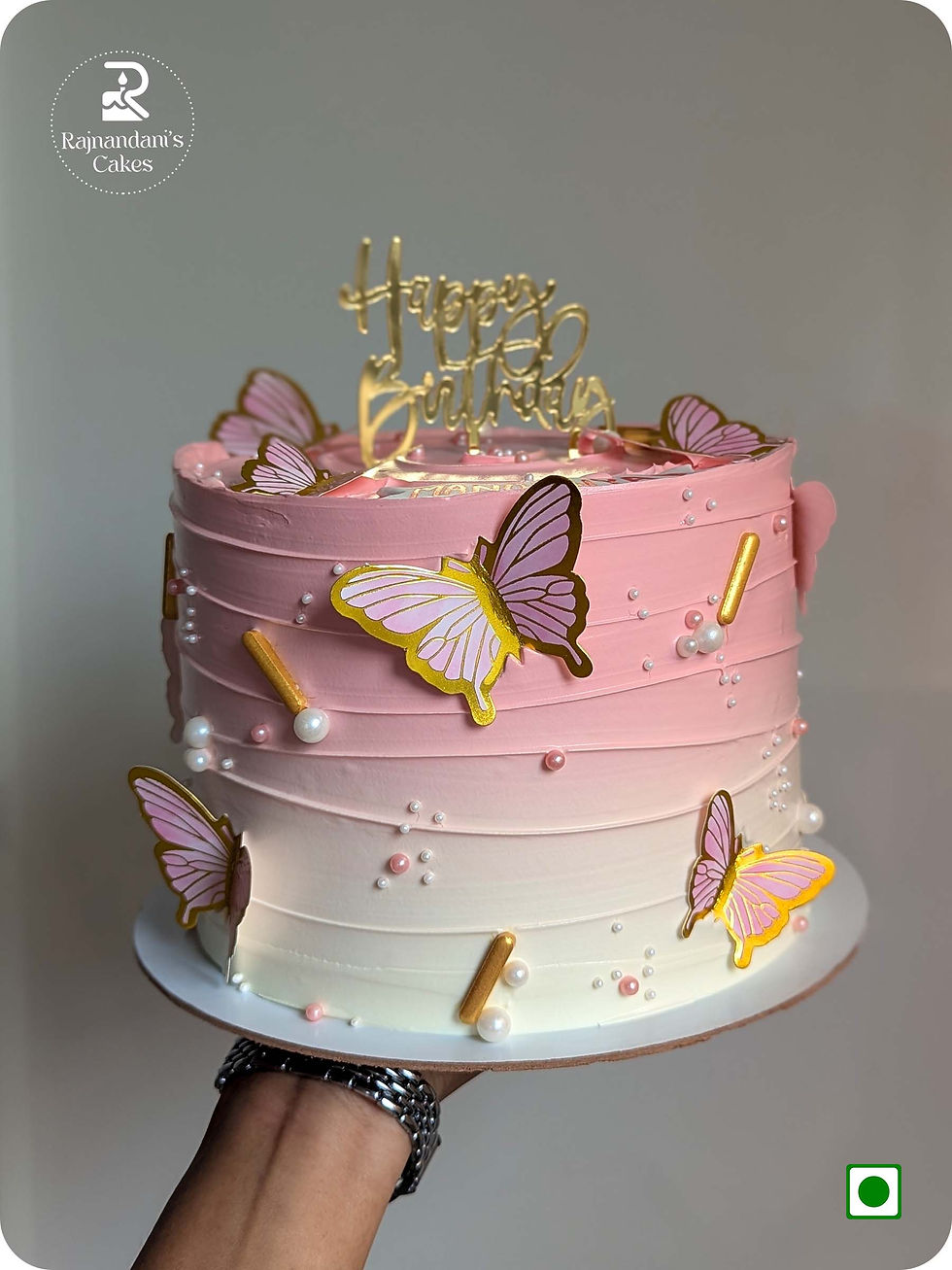 Pink and ivory textured birthday cake adorned with colorful butterfly cutouts and golden accents by Rajnandani's Cakes.
