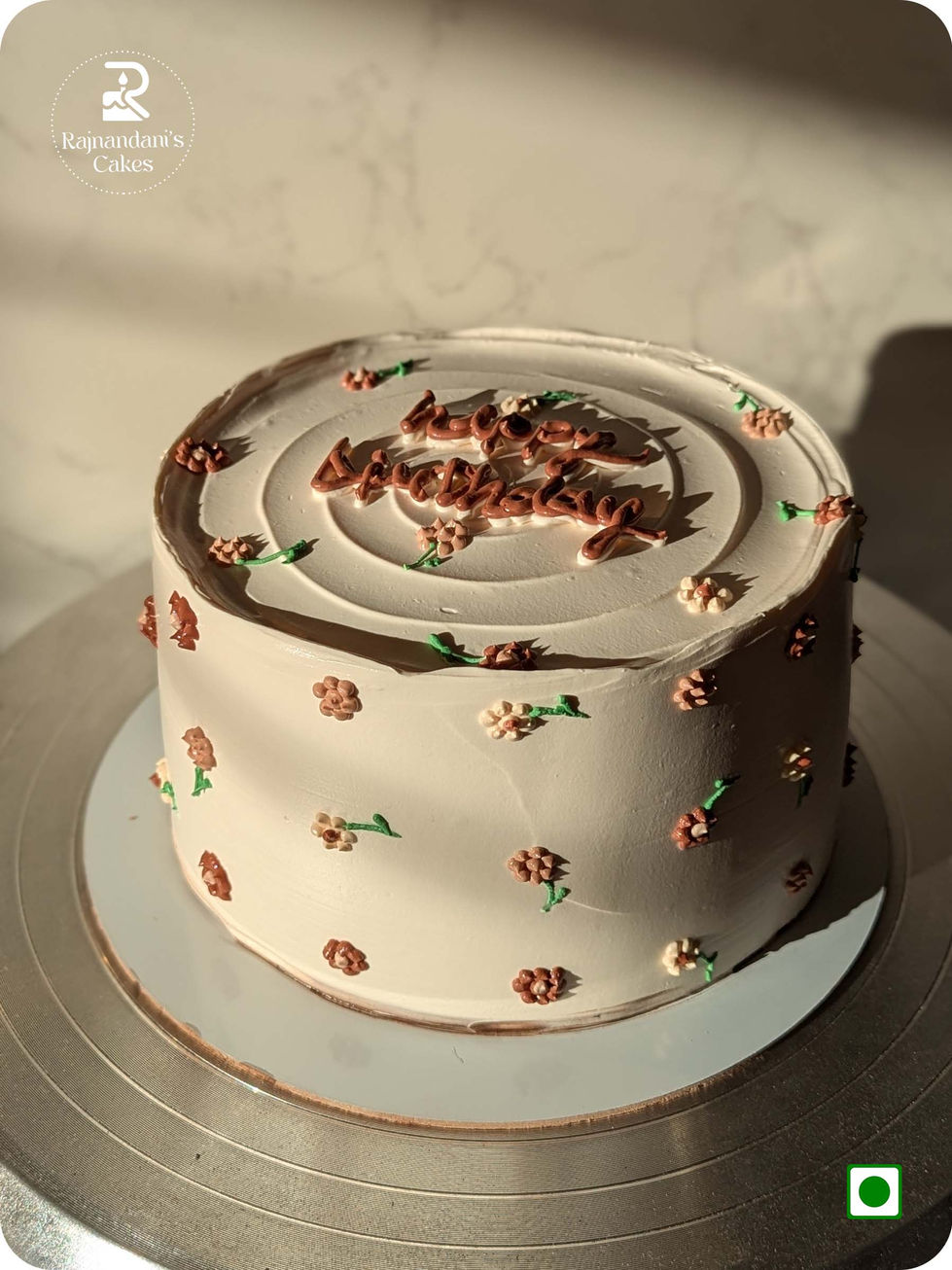 Textured round cake decorated with piped miniature flowers and cursive birthday message by Rajnandani's Cakes.
