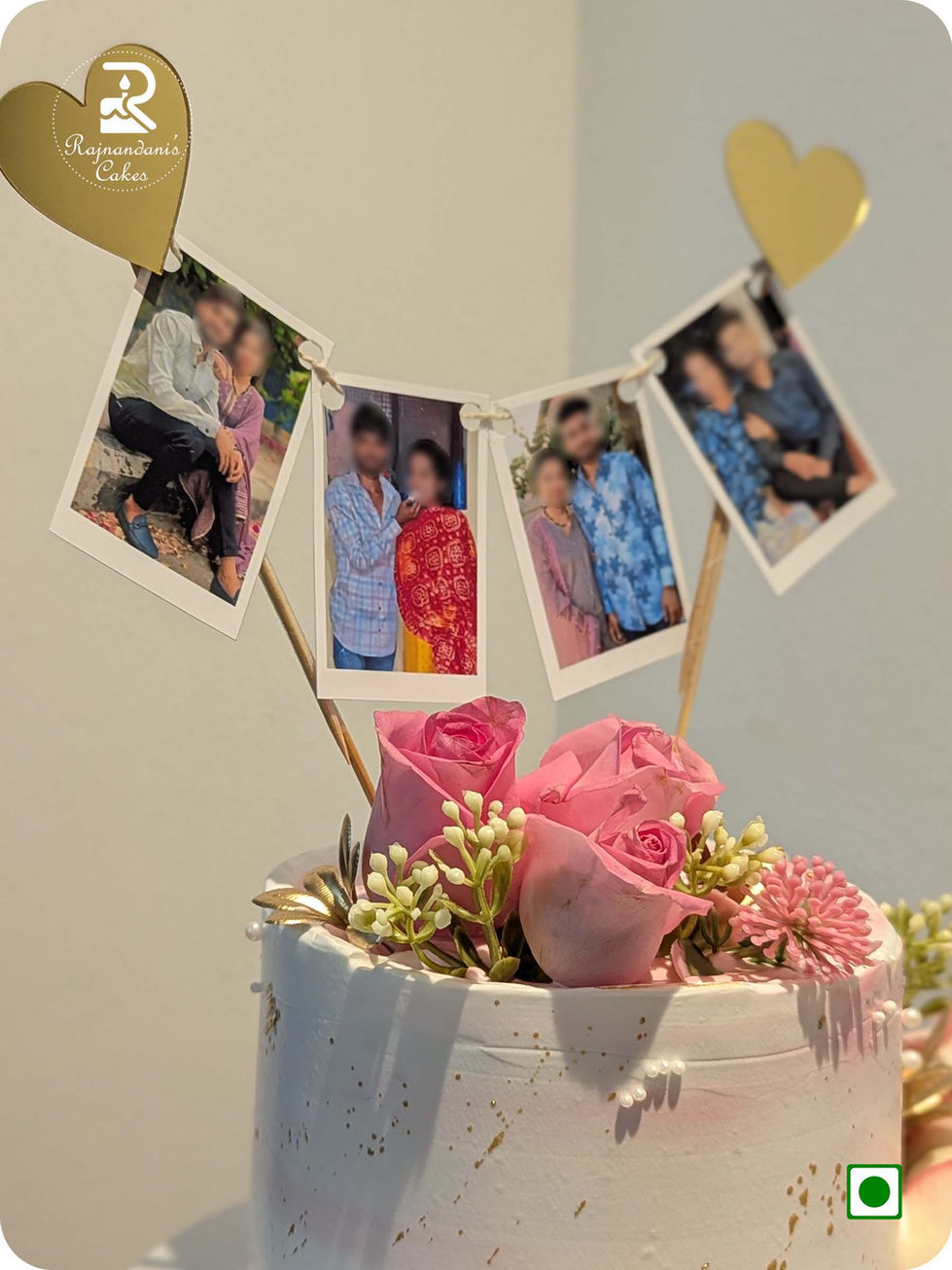 Elegant floral cake featuring hanging mini polaroid photo bunting, pink fresh roses, sugar pearls, and gold accents.