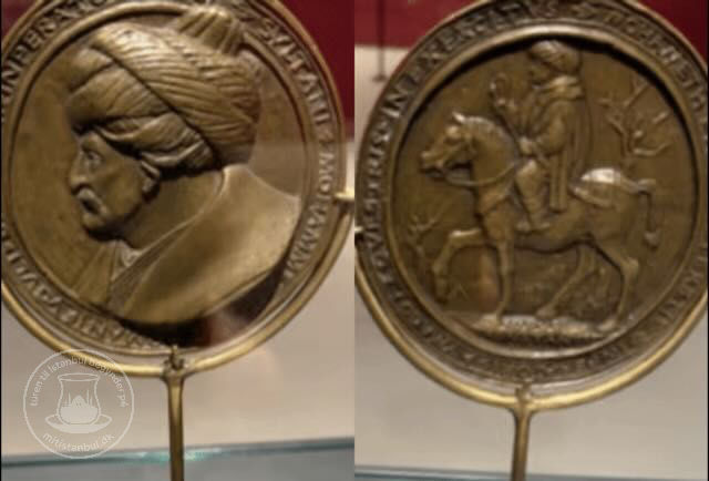 To medaljer med relief: venstre viser en mand med turban; højre viser en rytter på hest. Guld farve med indgraveret tekst på kanten.