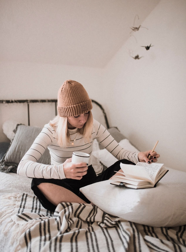 Woman reads book in bed with coffee