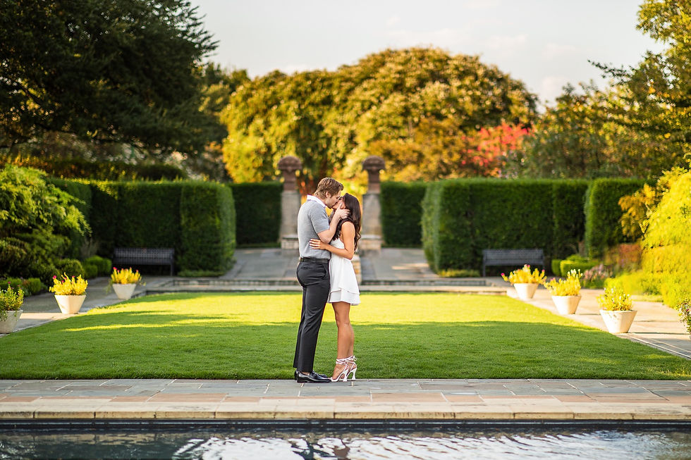 Proposal photoshoot. Couple embraces on lush garden lawn, surrounded by green hedges and trees. Bright, sunny day with vibrant colors and romantic mood.