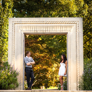 Engaged couple Kelcey Wetterberg and Nate Crnkovich standing under a stone arch in a garden during their engagement photoshoot.
