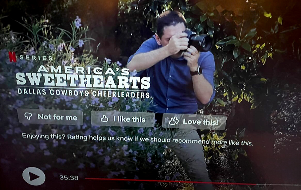 Man in blue shirt photographing in garden backdrop. Text: "America's Sweethearts: Dallas Cowboys Cheerleaders." Rating buttons displayed.