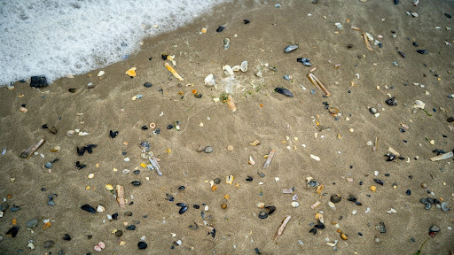 A cluster of white plastic nurdles and tangled synthetic fibers resting on a sandy beach.