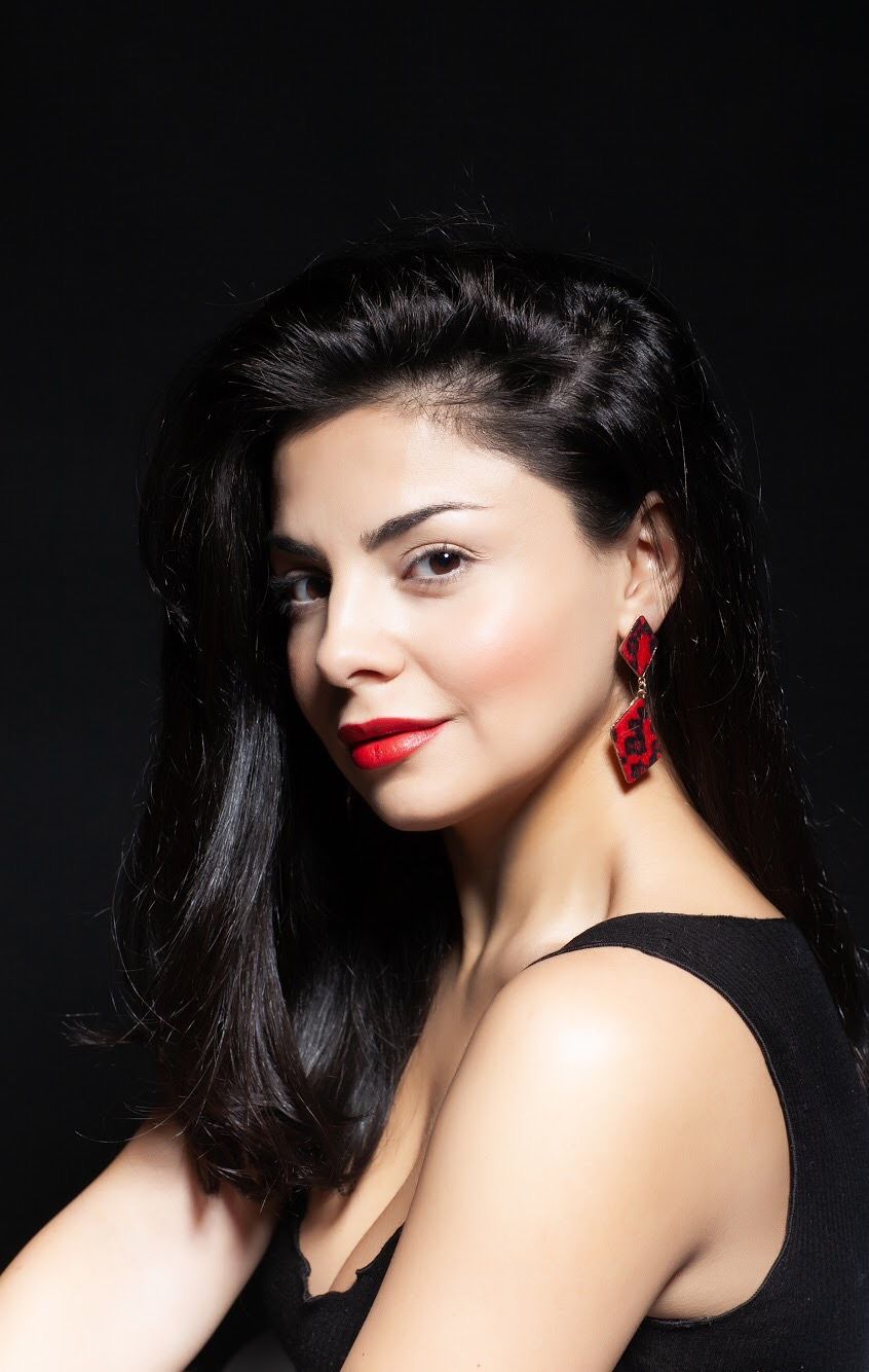 Glamorous side profile portrait with red lipstick and statement earrings against dark background.