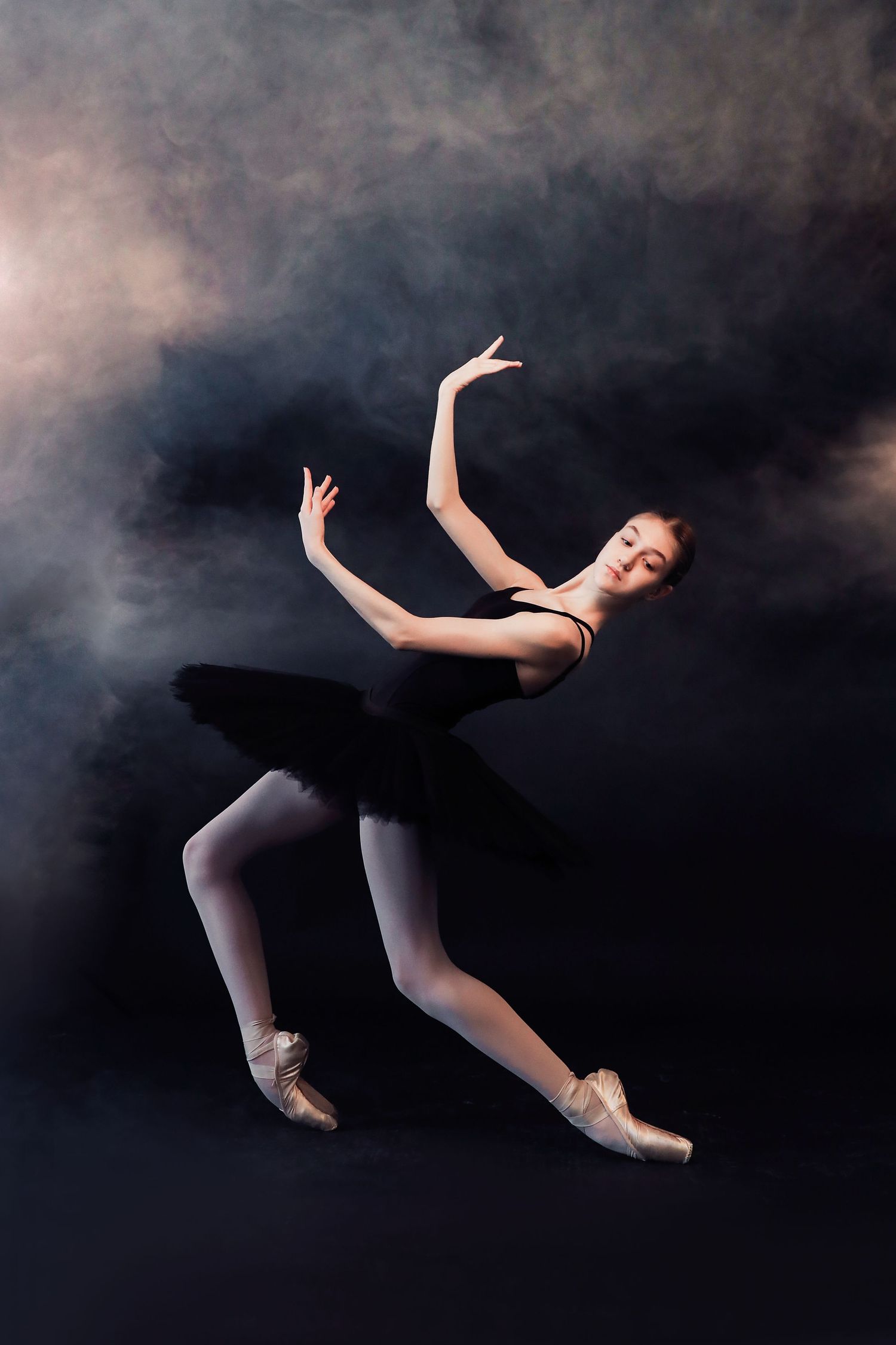 A ballet dancer in a black tutu performs a graceful leap against a dark smoky background.