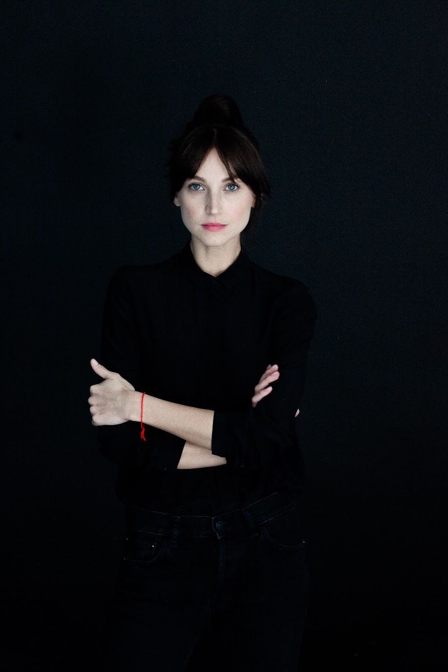 Minimalist portrait against black background wearing black turtleneck with arms crossed.