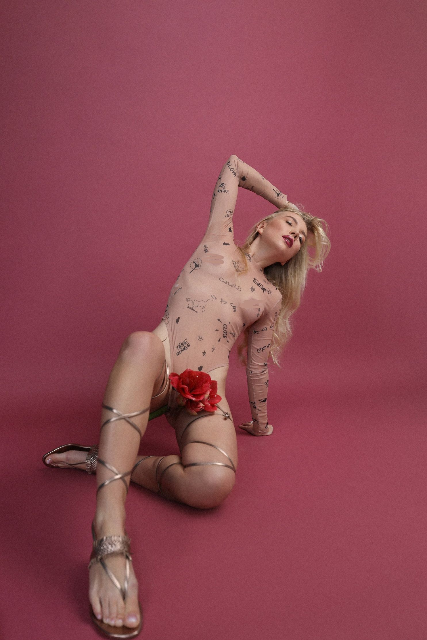 Artistic pose with floral details and strappy sandals against pink background.