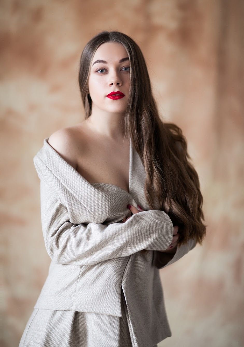 Portrait in soft lighting wearing an oversized beige sweater against a textured brown background.