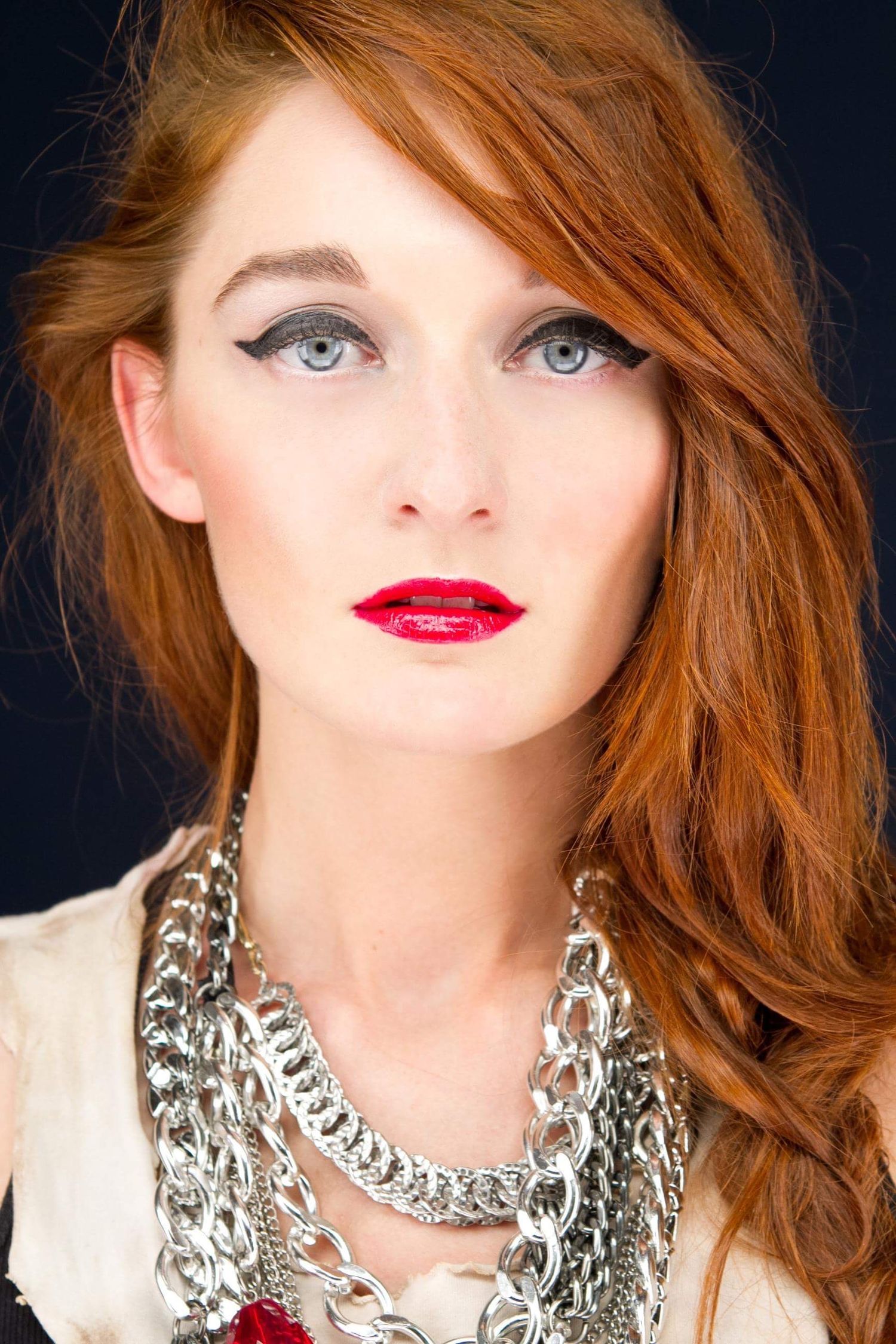 Beauty portrait featuring dramatic red lipstick, winged eyeliner and layered silver chain necklace.