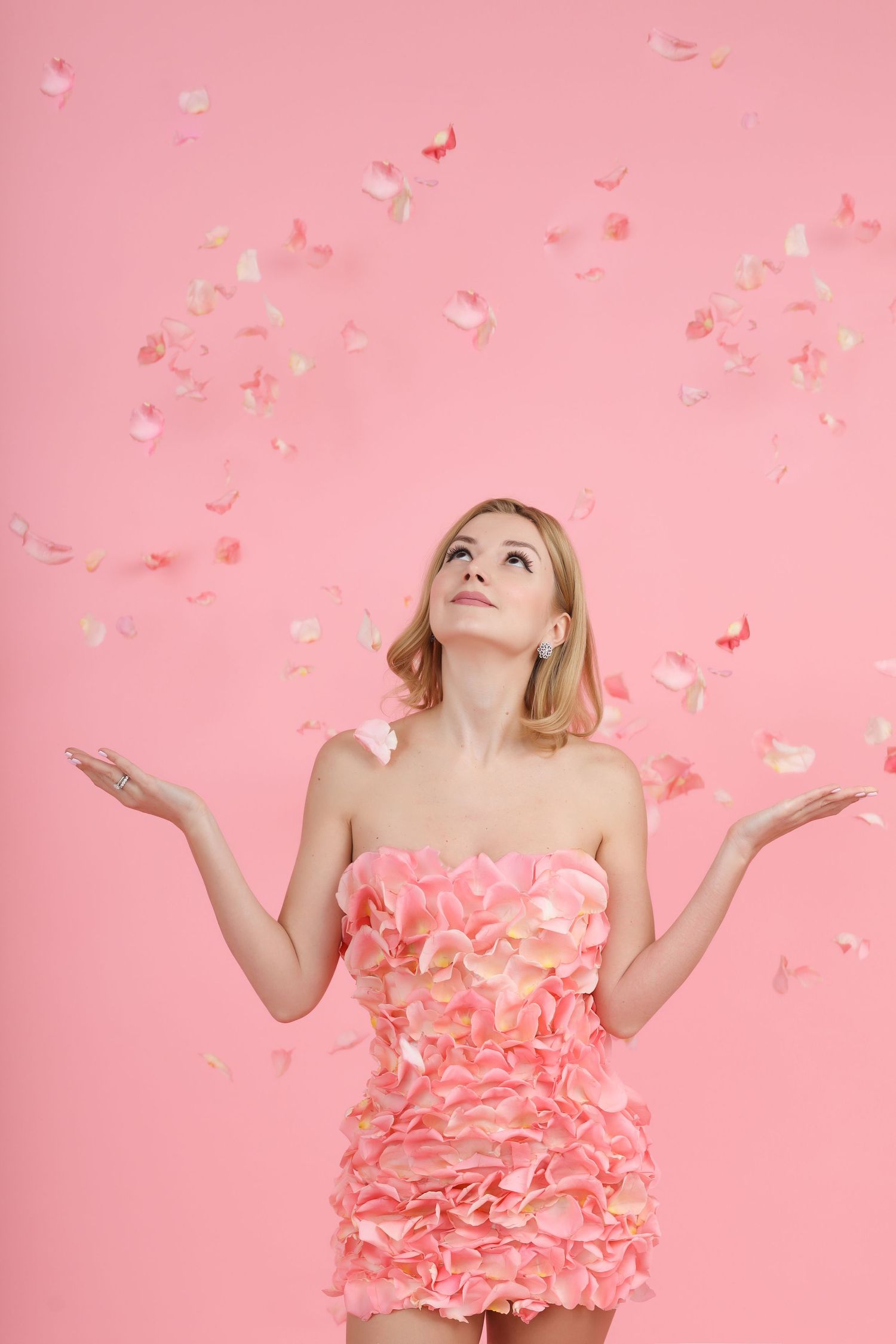 Pink floral dress made of petals with falling rose petals against pink background.